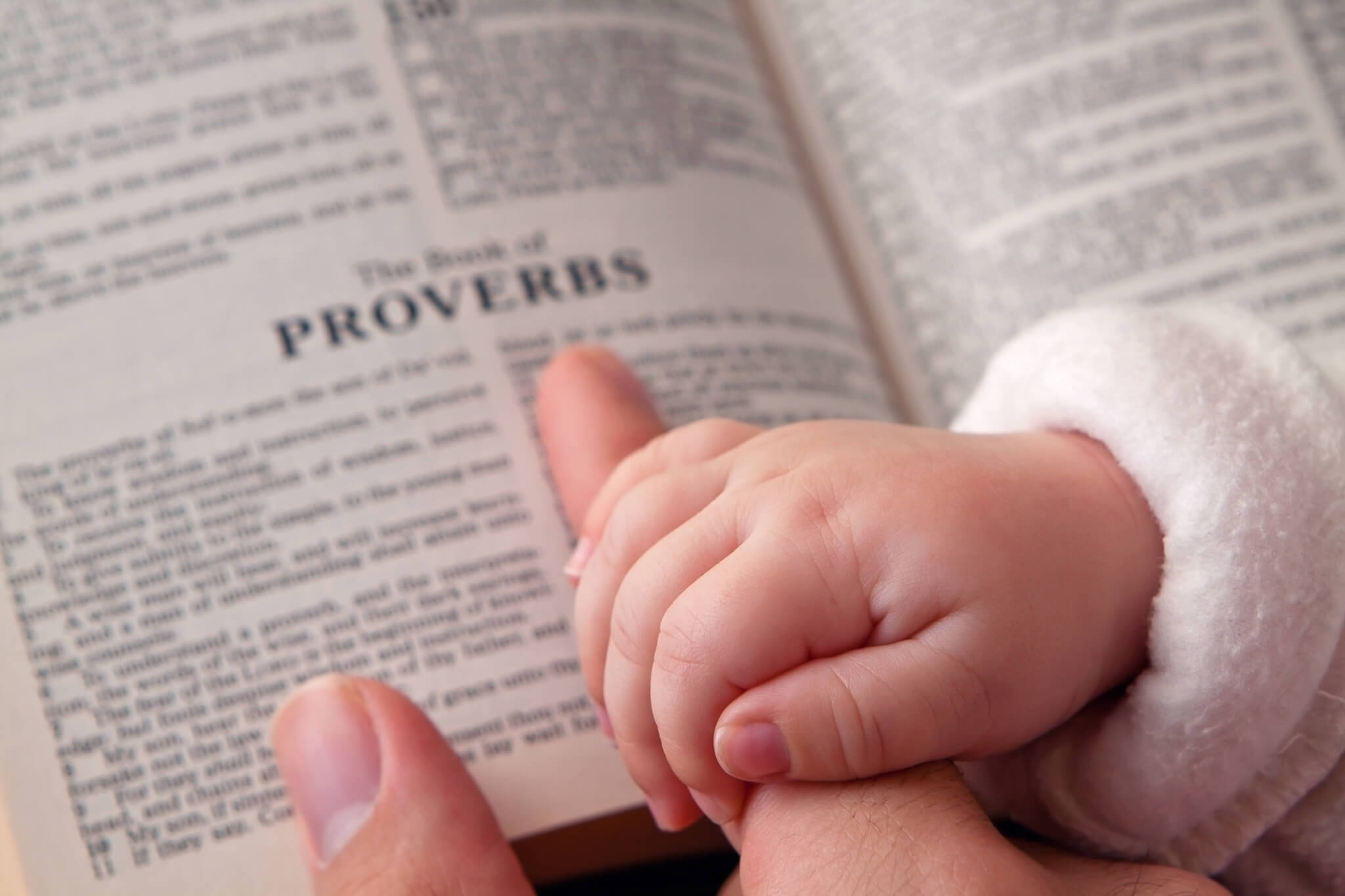Baby Holding Dad’s Finger on Bible