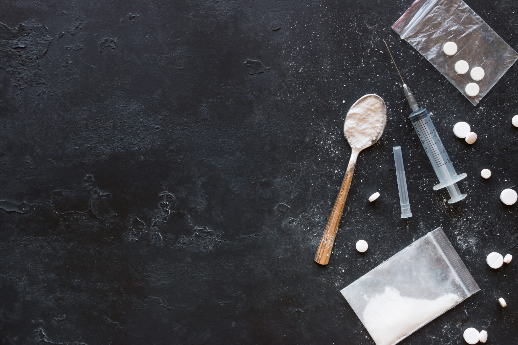 Drugs in the form of powder and tablets, a spoon and a syringe on a black background mockup