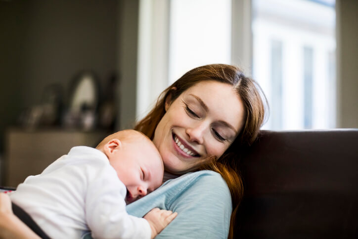 Smiling mother with sleeping newborn son on sofa